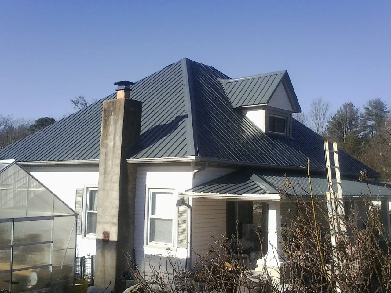 Dark blue standing seam metal roof on a white farmhouse with dormer — Slate & Tile Roof Repair by Roofing Brothers in Overton